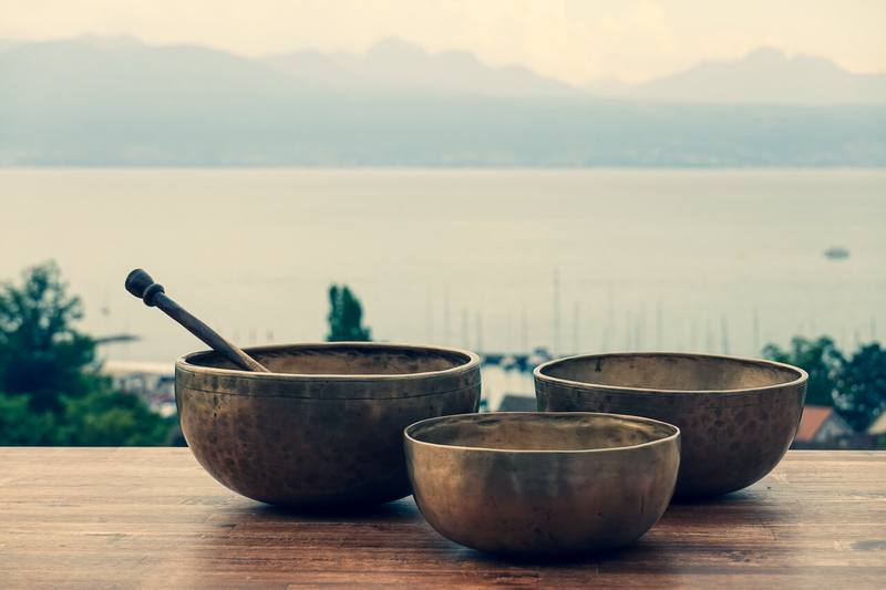 Trois bols chantants tibétains posés sur une table face au lac Léman